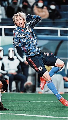 a man kicking a soccer ball on top of a field next to other people watching