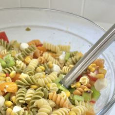 a glass bowl filled with pasta salad next to a silver spoon on top of a counter