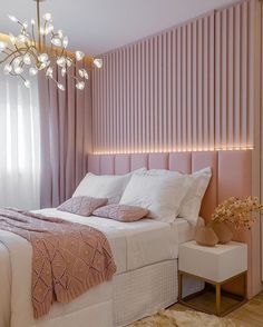 a bedroom with pink walls and white bedding in front of a chandelier