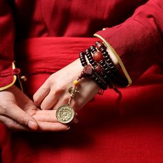 a woman in a red dress holding onto some bracelets and a gold coin on her wrist