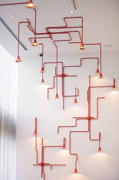 a white room with red pipes on the wall and lights hanging from it's ceiling