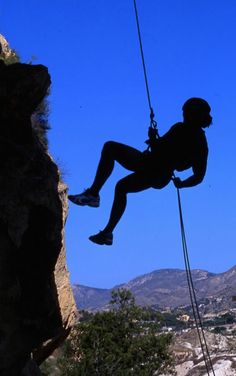 a man hanging off the side of a cliff while holding onto a rope with his feet