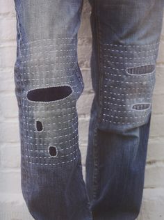 a person wearing blue jeans with holes in the bottom and sides, standing next to a white brick wall