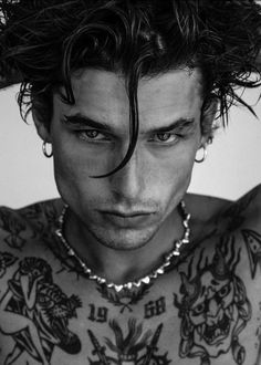 a man with tattoos and piercings on his chest is looking at the camera while holding his hair back