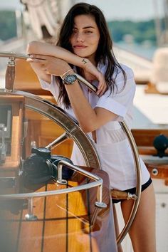 a beautiful young woman leaning on the side of a boat with her hand on the steering wheel