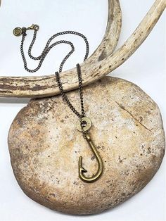 Fishing Necklace - Bullet Necklace - "Hooked on Shooting and Fishing" Necklace - Unisex Styling - Choice of LengthsAntique brass fish hook suspended from a cut bullet/rifle casing used as a ring connector.Hung on a matching antique brass curb chain. Lobster closure.Dimensions of fish hook: 1 3/4" long x 3/4" at widest point.Optional lengths. Use dropdown to make your selection. WANT IT IN STAINLESS STEEL INSTEAD? Choose in dropdown.A SureShot™ Jewelry exclusive.Brands and calibers vary. Contact Fishing Necklace, Adornment Jewelry, Bullet Necklace, Hook Necklace, Bullet Jewelry, Fish Necklace, Money Clips, Brass Hook, Push Pins