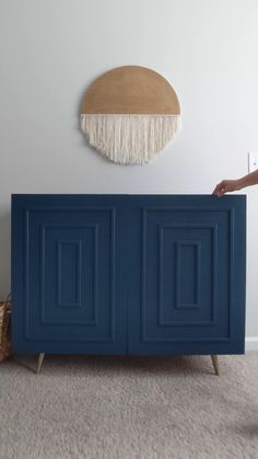 a blue cabinet with fringe hanging on the wall next to a wicker basket and rug