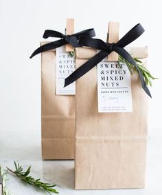 two brown paper bags with black ribbon tied around them on a white surface next to some herbs