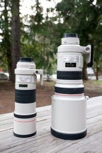 two large cameras sitting next to each other on a wooden table in front of trees