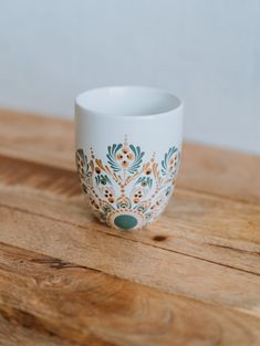 a white coffee cup sitting on top of a wooden table covered in green and gold designs