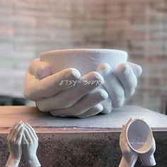 two hands holding a white bowl on top of a wooden table next to other objects