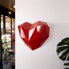 a red heart shaped object mounted to the side of a white wall next to a green plant