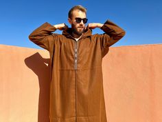 Beautiful Moroccan brown coat for men made in a warm, soft and thick fabric. This traditional djellaba will be very pleasant to wear everywhere (indoors and outdoors,...) when the temperatures drop. This men's djellaba has a neckline, long sleeves and a large rigid hood to protect you from the cold wind but from the sun too. Very quick to put on, ample, airy and which does not stick to the skin this Moroccan garment is a real plus to have as its comfort characterizes it. This traditional dress will adapt perfectly to different morphologies because of its shape (dimensions at the bottom of the description). - Thick soft fabric that does not crease - Item Weight: kg - Color: brown  - brown and white embroidered neckline - Large hood - Dimensions: Width under the arms (flat): 71 centimeters = Moroccan Clothing, Coat For Men, Embroidered Neckline, Brown Coat, Thick Fabric, Traditional Dress, Traditional Dresses, Put On, Mens Coats