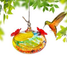 a glass ornament hanging from a tree branch with a hummingbird flying next to it