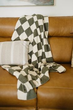 a couch with a checkered blanket on top of it next to a brown leather chair