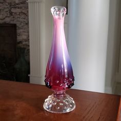 a pink and purple vase sitting on top of a wooden table next to a fireplace