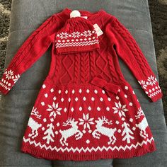 a red sweater dress with white snowflakes and reindeers on it, sitting on a couch