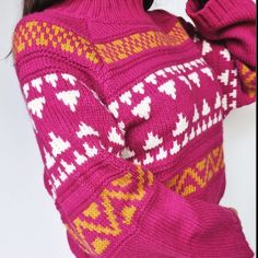 a woman is wearing a pink sweater with yellow and white designs on the sleeves, she has her hands behind her head