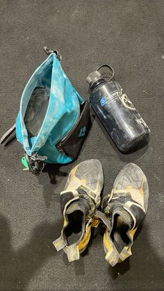 two pairs of shoes and a water bottle are on the ground next to a bag