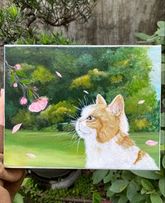 a person holding up a painting of a cat in front of some bushes and trees