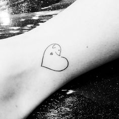 a small heart tattoo on the foot of a person's leg, with water in the background