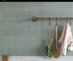 the wall is made up of green tiles and wooden utensils hanging from hooks