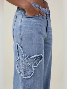 a person wearing blue jeans with butterfly appliques on the side and back pocket