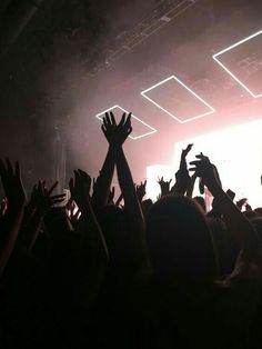 a crowd of people at a concert with their hands in the air and lights shining down on them