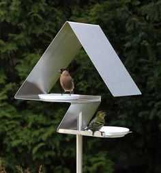 a bird sitting on top of a metal object in the middle of a field next to trees