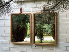 two mirrors hanging on the side of a brick wall next to a pine tree branch