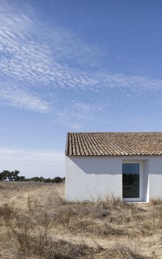 a small white building sitting in the middle of a dry grass field