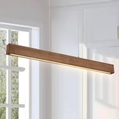 a wooden light fixture hanging from the ceiling in a room with white walls and windows