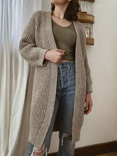 a woman standing in front of a window wearing ripped jeans and a cardigan sweater