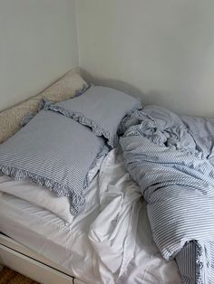 an unmade bed with blue and white striped sheets