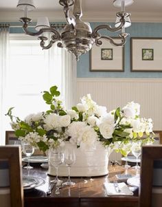 a dining room table with white flowers in a vase on it and pictures hanging above the table