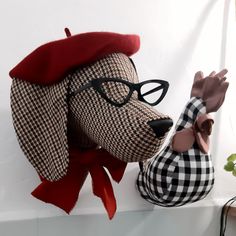 a stuffed dog wearing glasses and a red hat on top of a white shelf next to a potted plant