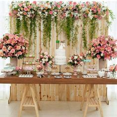 a table topped with lots of pink and white flowers next to a wall covered in greenery