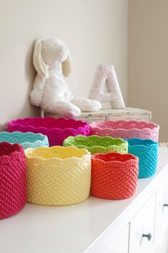 colorful knitted baskets sit on top of a white dresser next to a stuffed animal