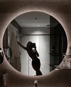 a woman taking a selfie in front of a bathroom mirror with the lights on