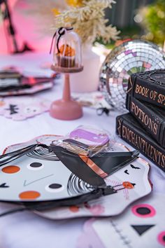 a table topped with books and plates covered in halloween themed paper mache decorations on top of a white table cloth