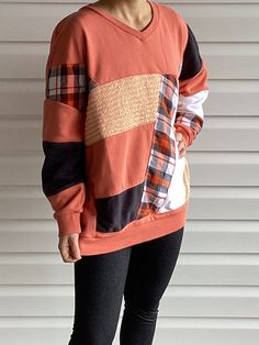 a woman standing in front of a white wall wearing an orange sweater and black leggings