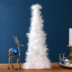 a tall white feather christmas tree next to a blue and gold ornament on a wooden table