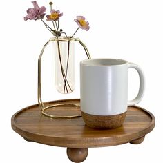 a white coffee cup sitting on top of a wooden table next to a vase with flowers in it