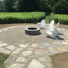 two white adiron chairs sitting on top of a gravel covered field next to a fire pit