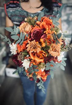 a woman holding a bouquet of orange and red flowers with greenery in her hands