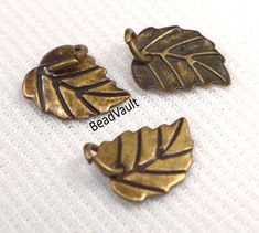 three brass leaf charms sitting on top of a white cloth