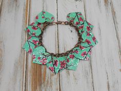 a green bracelet with pink flowers on it and a chain hanging from the clasps