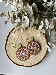 two brown and white flower shaped earrings sitting on top of a wooden slice next to flowers