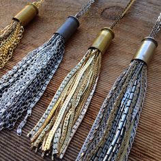 four different types of tassels on a wooden surface with gold chains and black beads