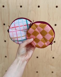 a hand is holding a small pink and yellow checkered purse with zippered closure